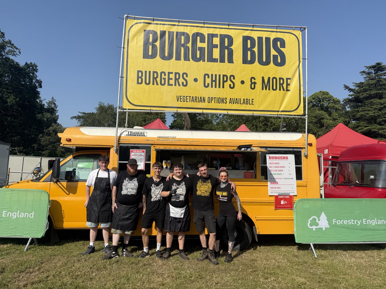 Burger Bus crew lined up in front of the yellow bus at a festival