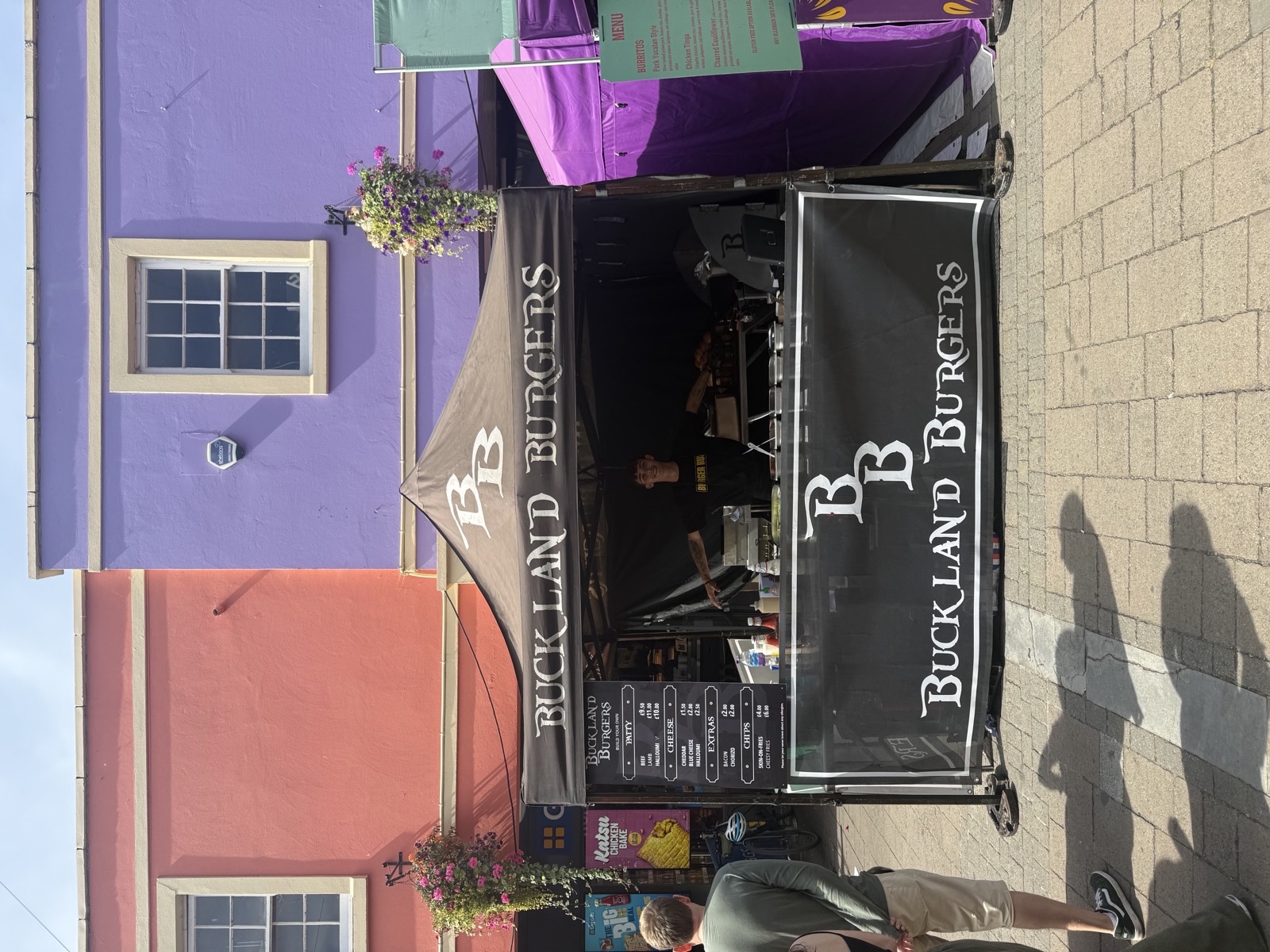 Tyler smiling with arms spread behind the Buckland Burgers stall counter